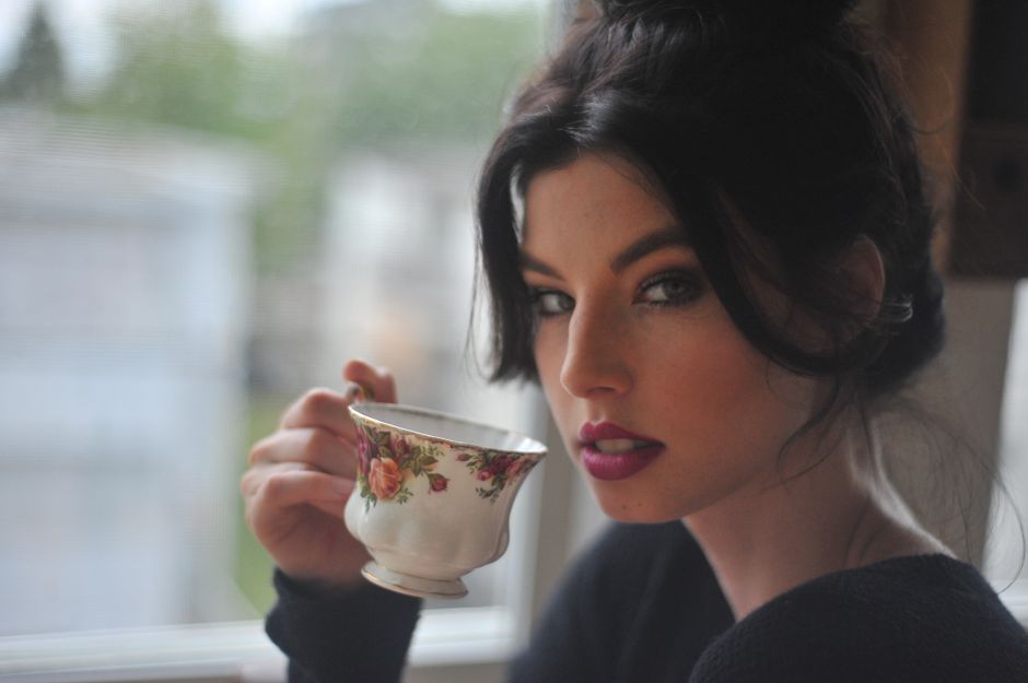 A woman in natural light enjoying tea near a window, elegant and serene vibe.