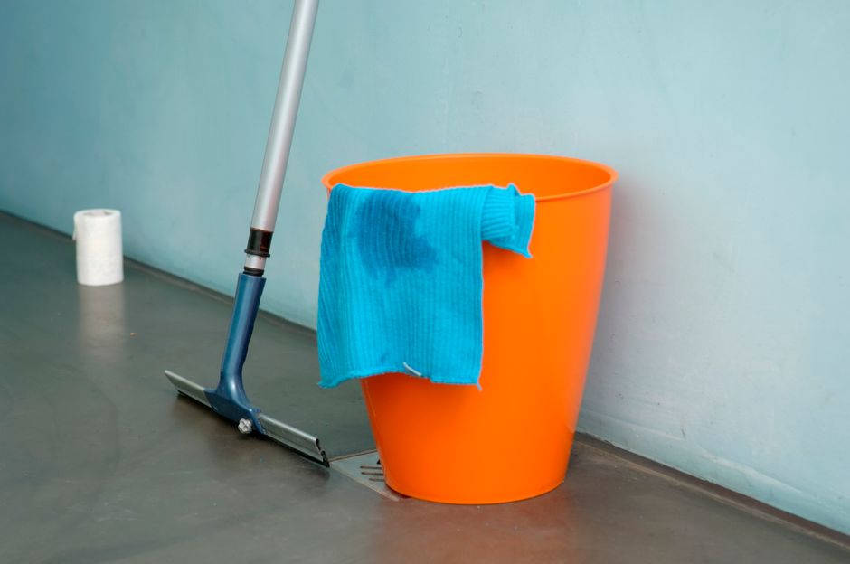Close-up of cleaning supplies including orange bucket, mop, and blue rag indoors.