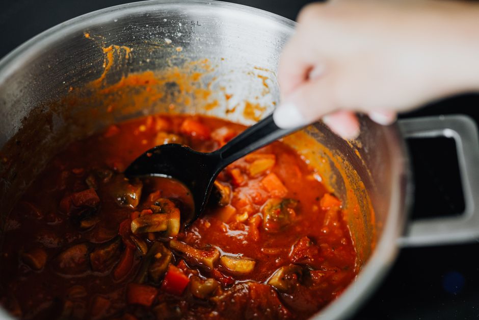 Freshly cooked vegetable stew with tomatoes and spices in a pot, stirred by hand.